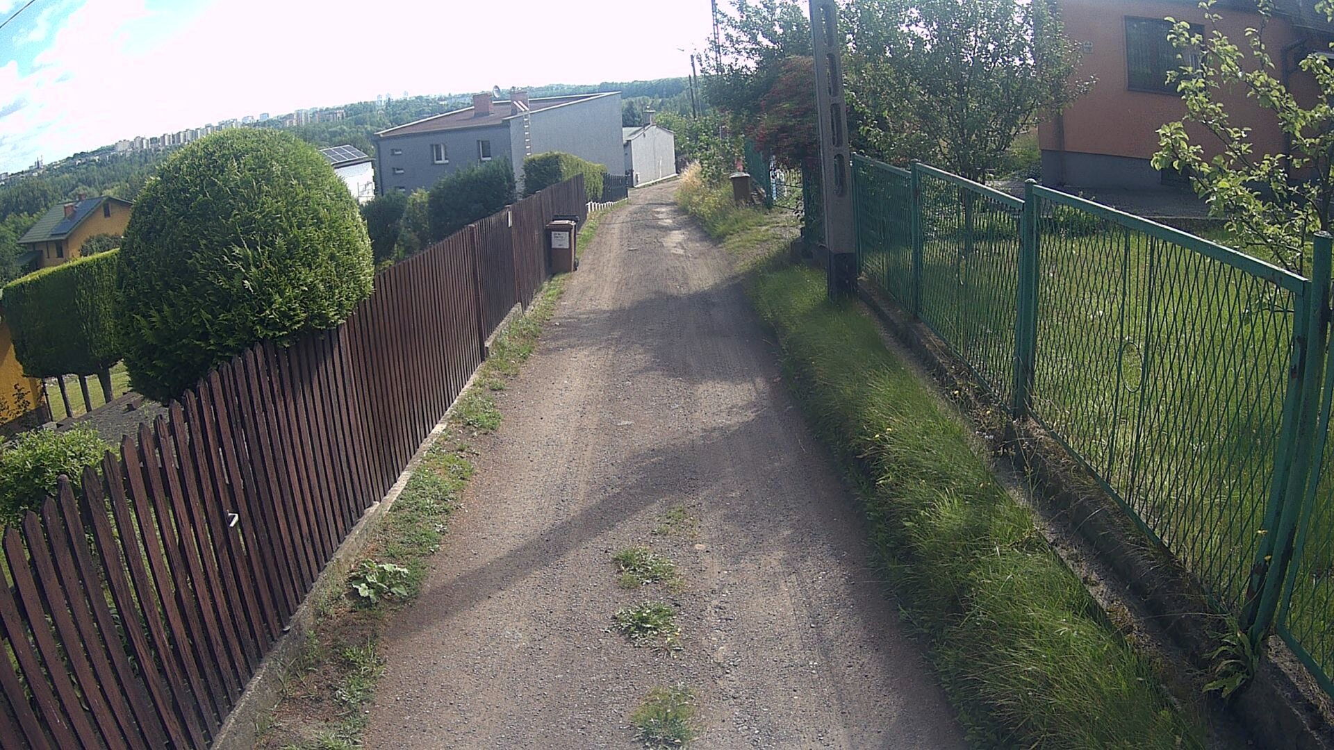 Droga gruntowa, płoty, budynki, trawa i drzewa.