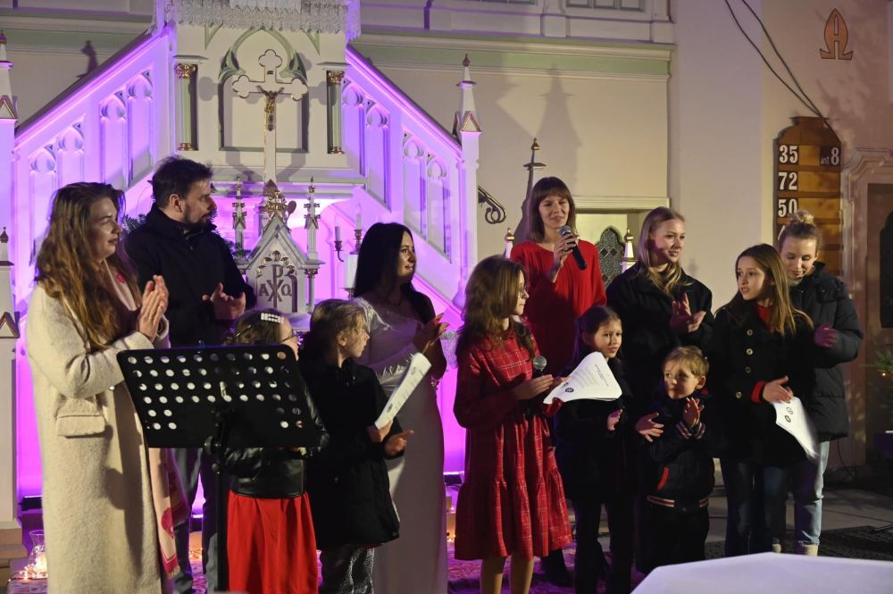 w kościele grupa osób stoi i klaszcze, jedna kobieta śpiewa do mikrofonu