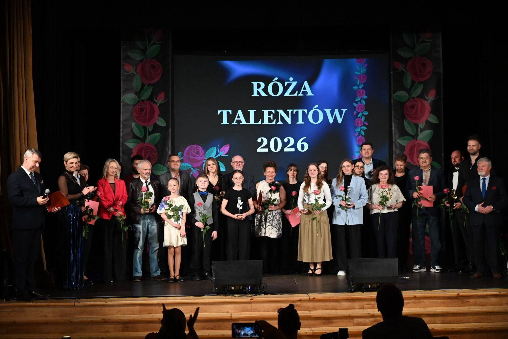 Na scenie stoi bardzo duża grupa ludzi - część trzyma róże. Z tyłu napis Róża talentów.