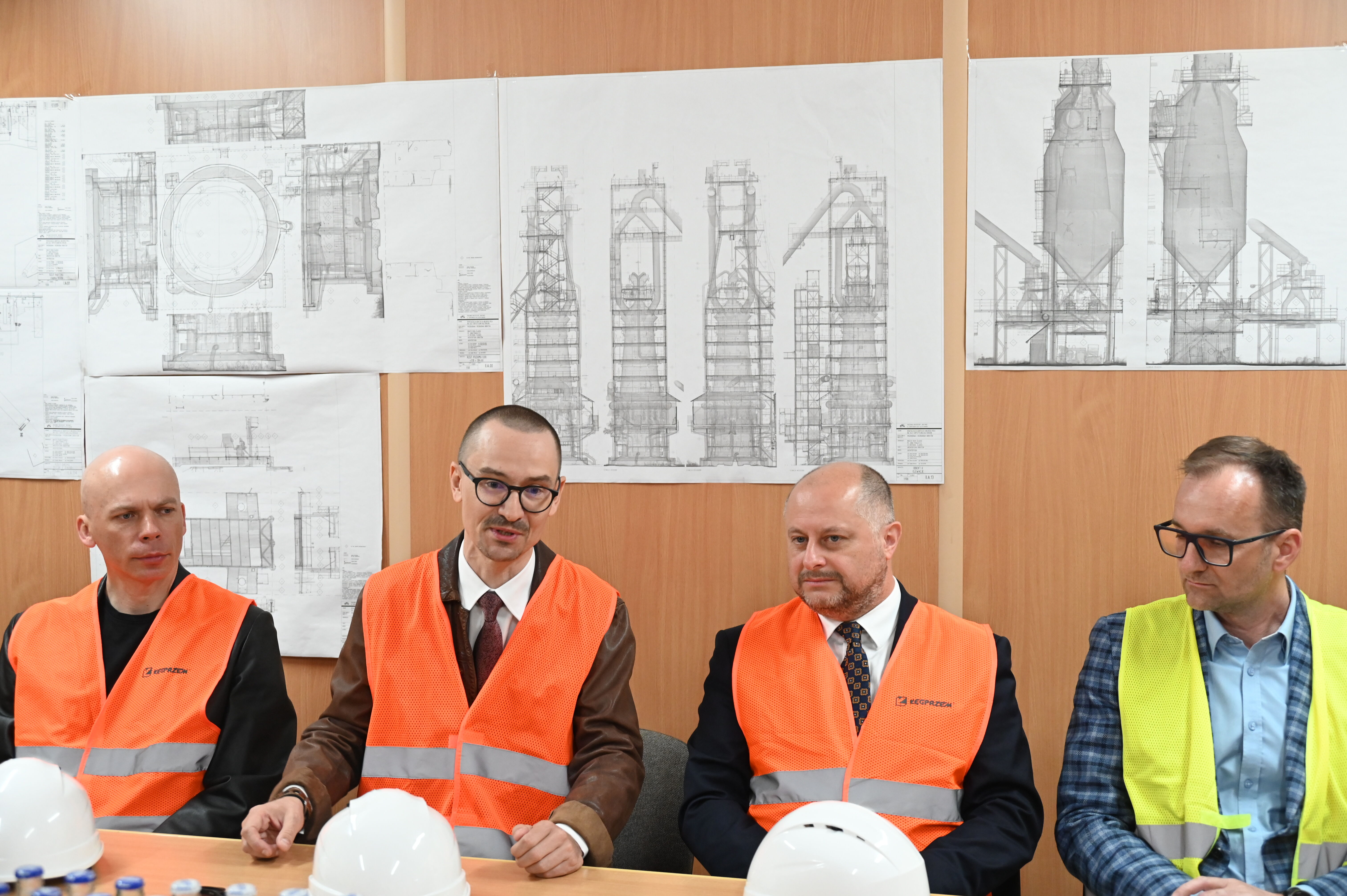 czterech mężczyzn siedzi przy stole w kamizelkach
