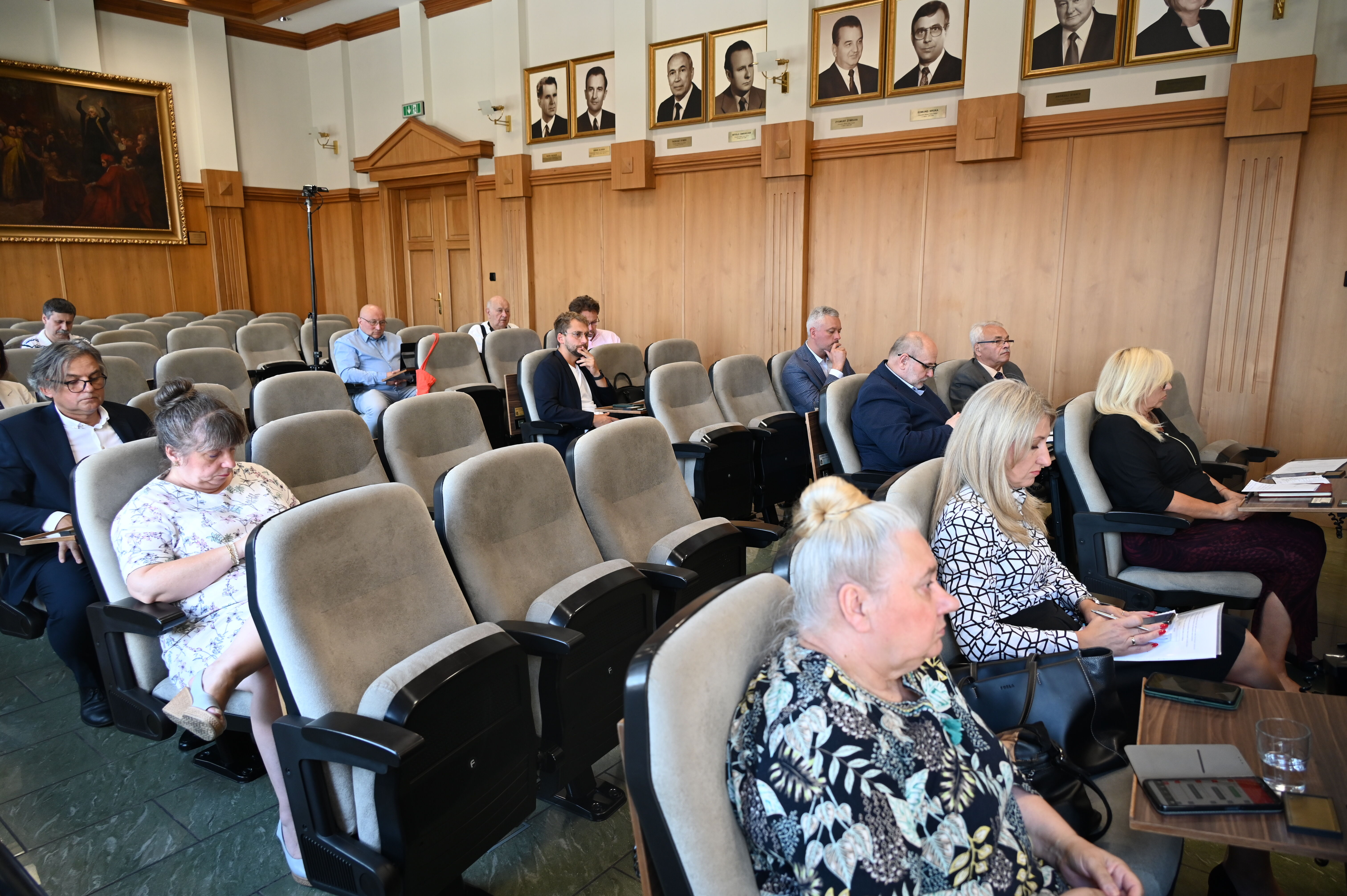 Wnętrze sali. Na fotelach siedzi grupa osób - kobiet i mężczyzn.