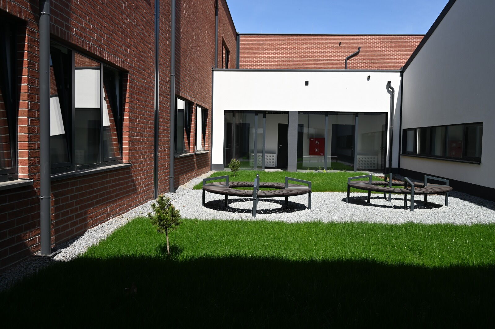 Trawnik, siedziska, budynek z przeszklonym wejściem.