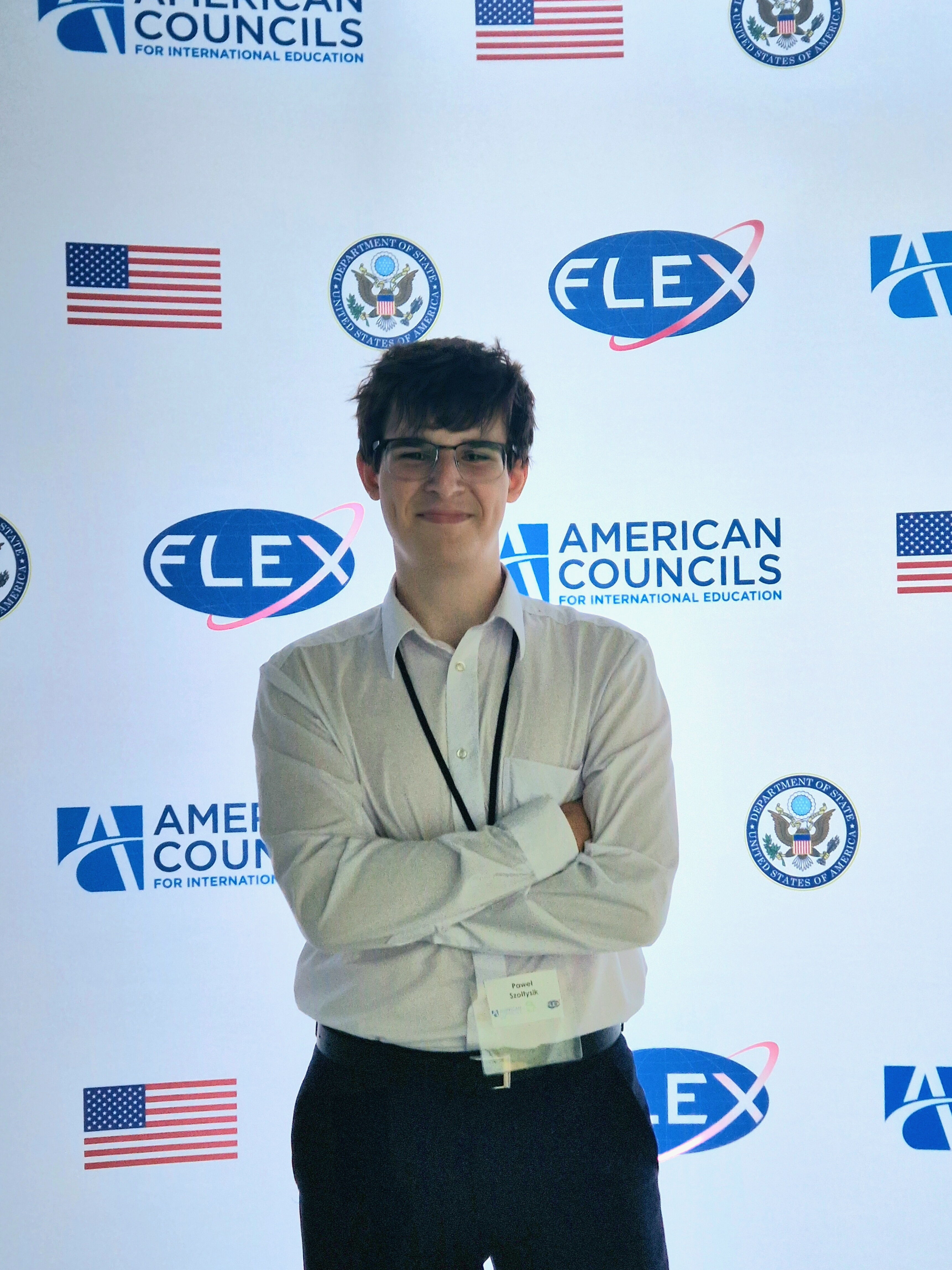 Chłopak pozujący do zdjęcia na ściance z nazwą programu.