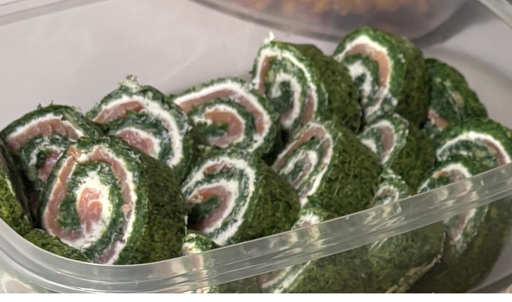 roladki z ciasta szpinakowego z łososiem poukładane w przeźroczystym pojemniku