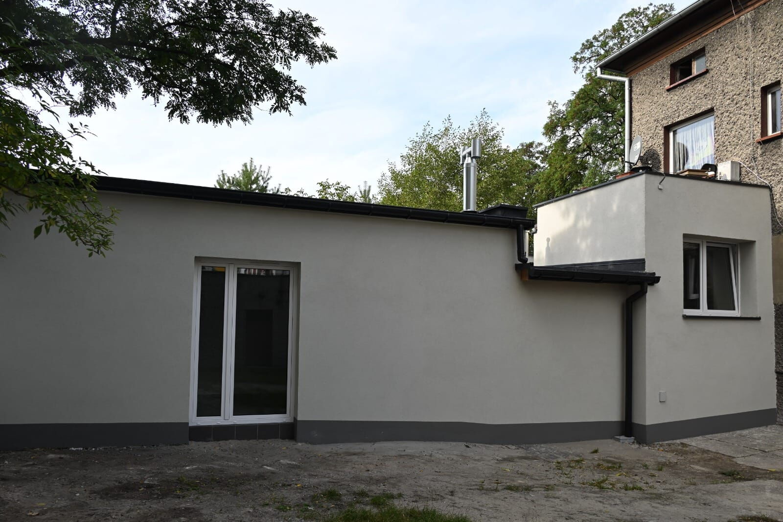 Parterowy budynek, w tle piętrowy budynek i drzewa.