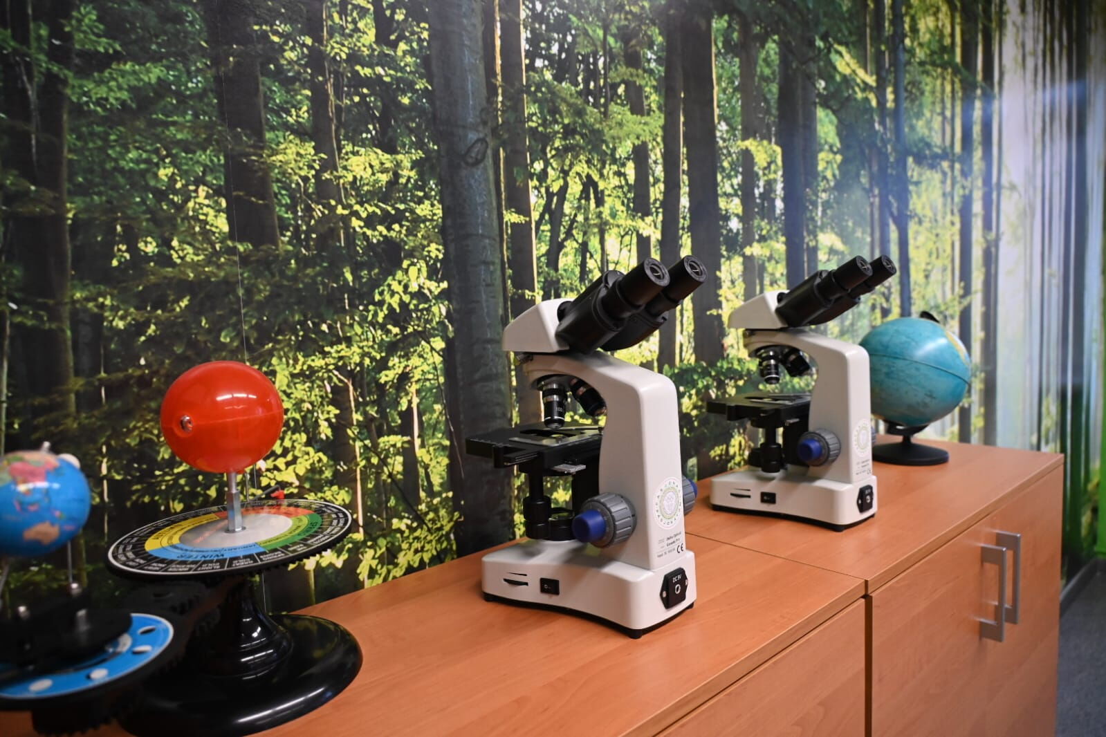 Wnętrze klasy - na szafce stoją mikroskopy oraz inne przyrządy. Na ścianie tapeta.