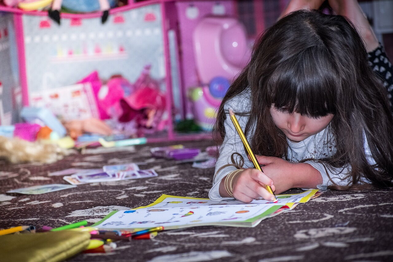 Dziewczynka rysujca w książeczce na dywanie.