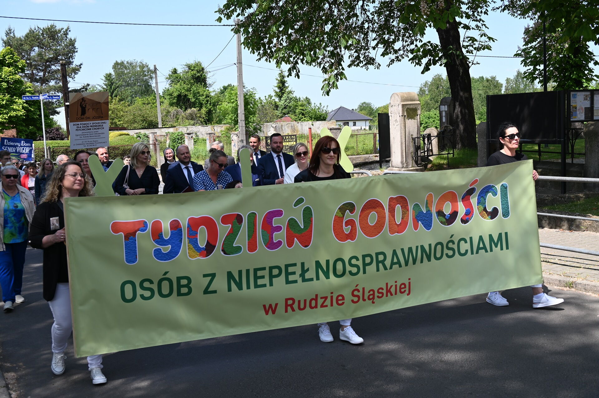 Grupa osób idzie w pochodzie, pierwsza trójka trzyma baner z napisem tydzień godności osób z niepełnosprawnościami w Rudzie Śląskiej