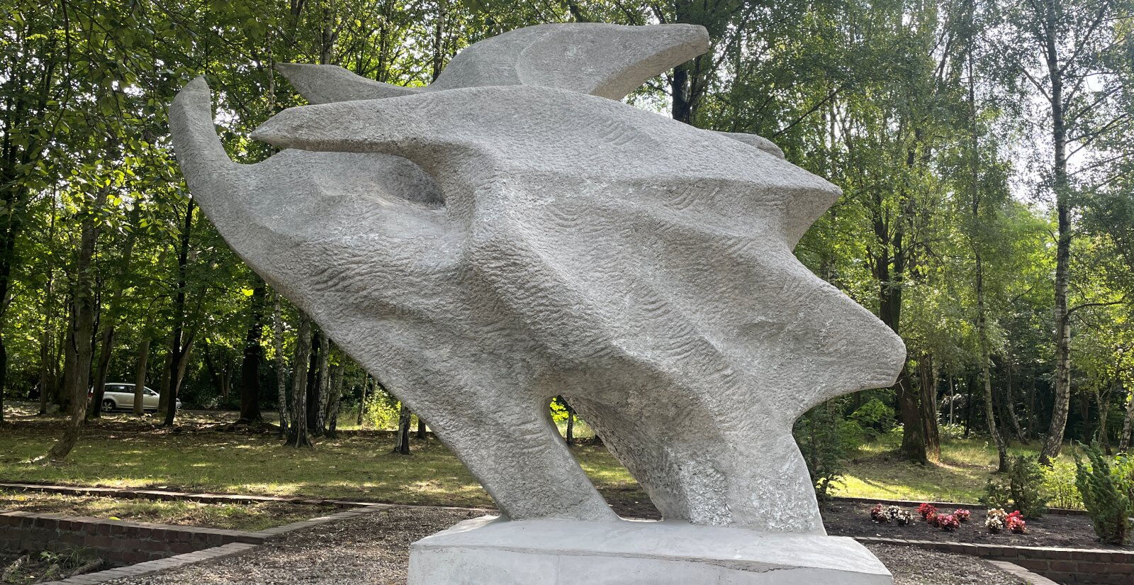 Rzeźba przedstawiająca ptaki wzbijające się do lotu, wokół drzewa i zieleń.