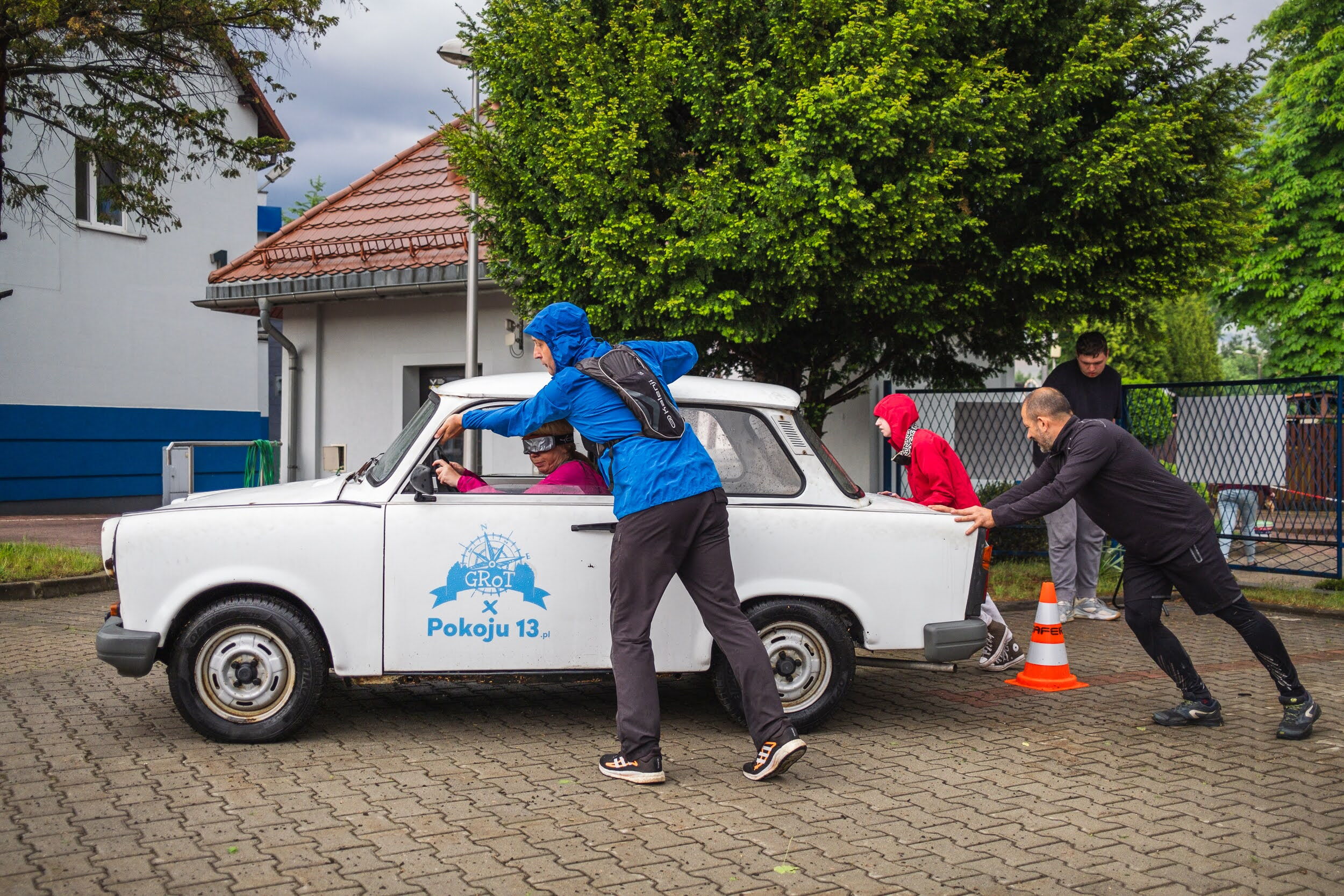 Grupa osób pcha auto z napisem Grot.