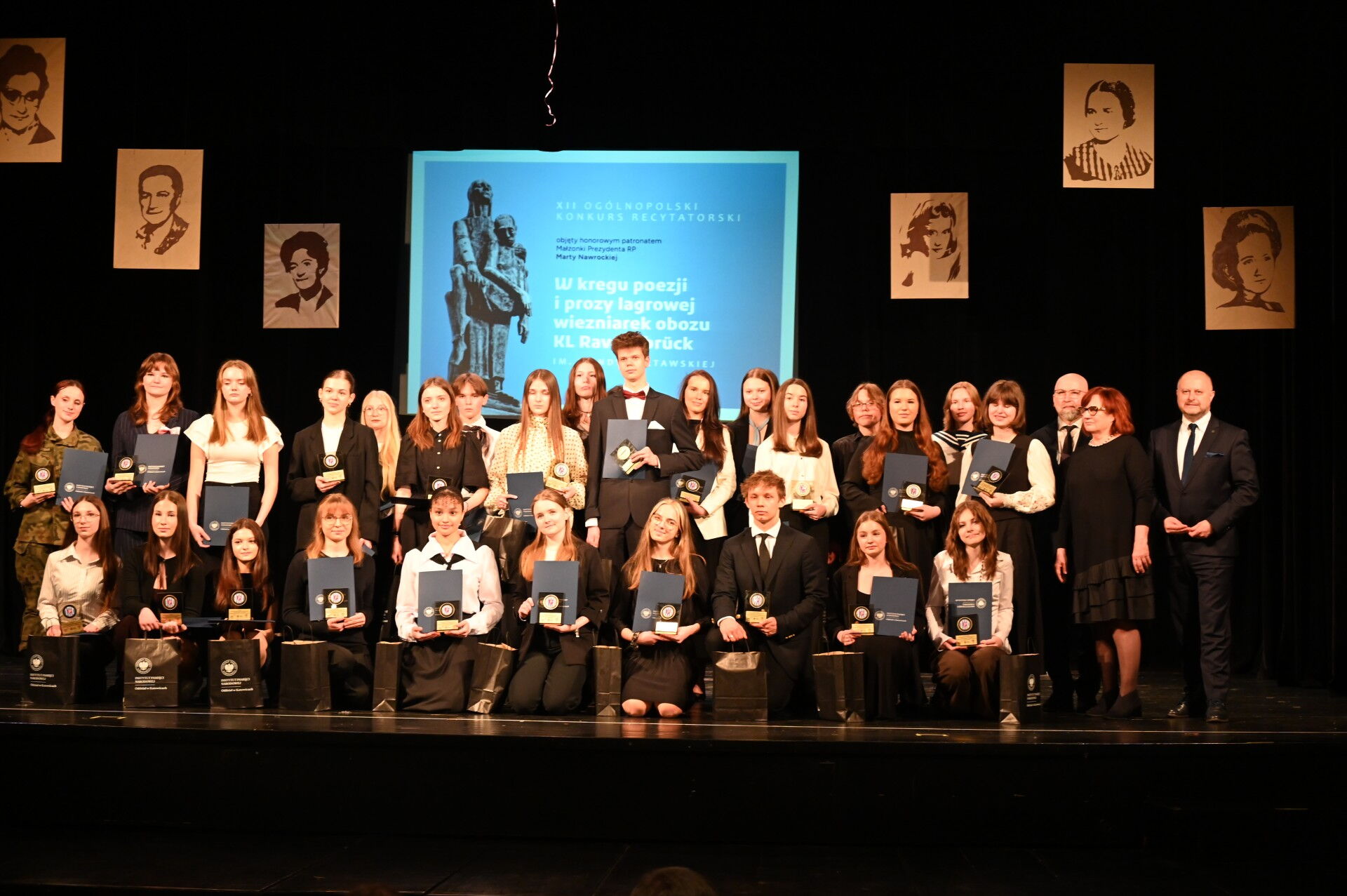 grupa osób na scenie prezentuje dyplomy i statuetki