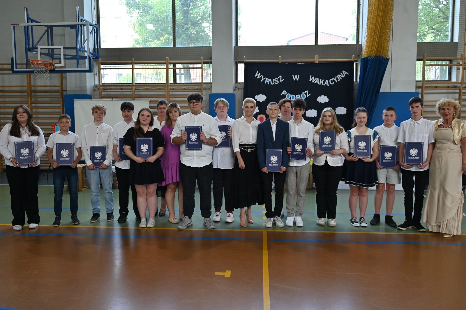 Grupa uczniów ze świadectwami w ręce pozuje do zdjęcia.