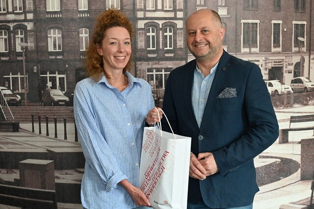 Kobieta i mężczyzna stoją na tle fototapety przedstawiającej stare kamienice.