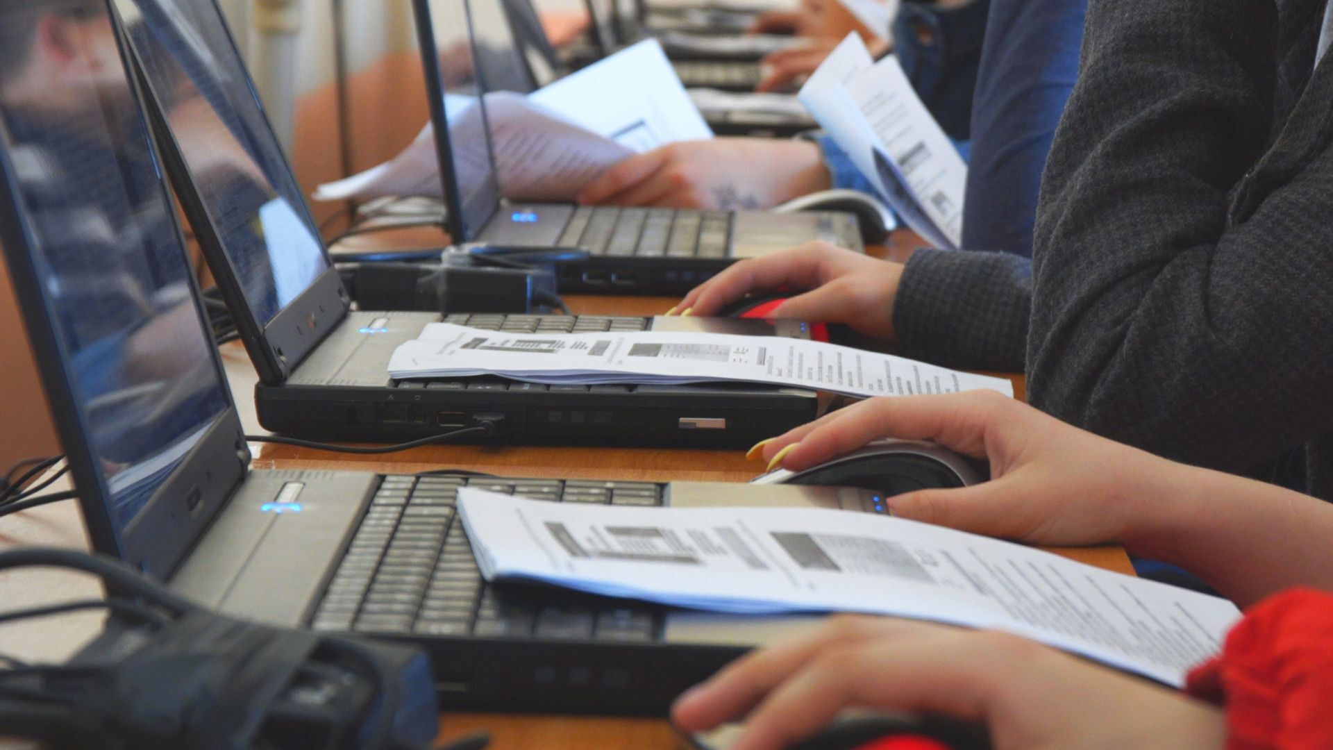 Laptopy, ręce siedzących przy nich osób, wydruki.