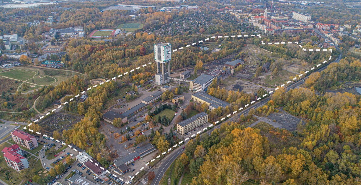 Widok z góry na tereny po kopalni Pokój. Na środku wieża wyciągowa, wokół budynki, dużo zieleni.