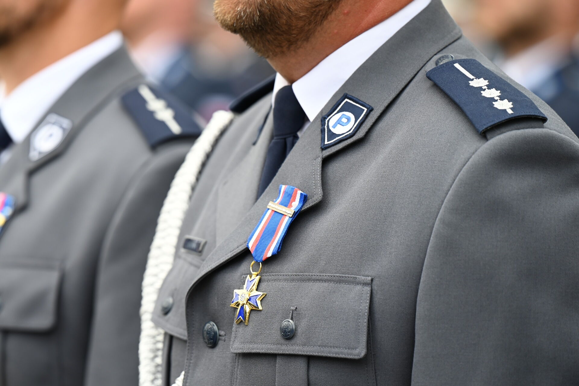 Fragment sylwetki w mundurze policyjnym z przypiętym medalem.