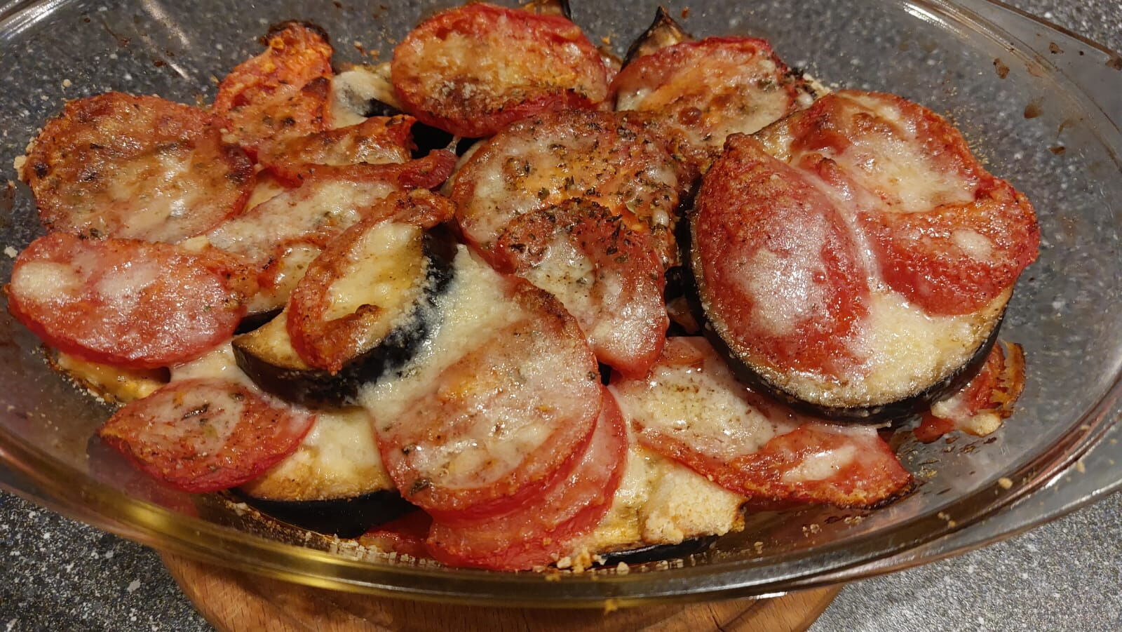 zdjęcie zapiekanki z pomidorów i bakłażana, posypanej serem  w przeźroczystym naczyniu żaroodpornym