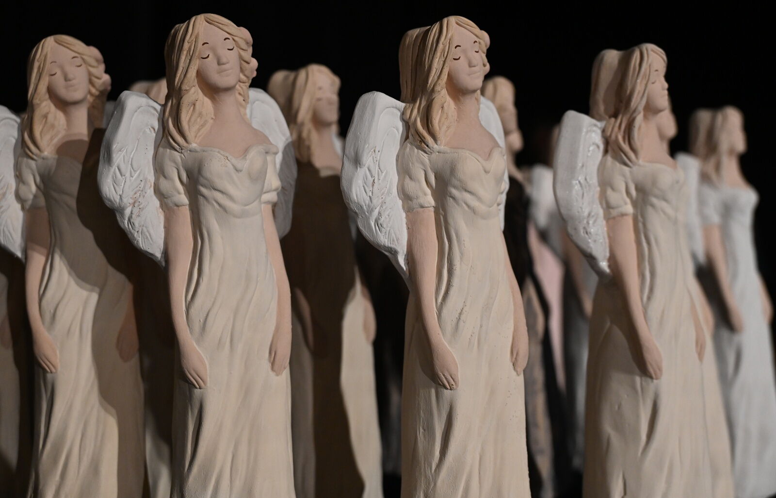 Statuetki przedstawiające postaci kobiet z długimi blond włosami, w długich beżowych sukniach, z białymi skrzydłami.