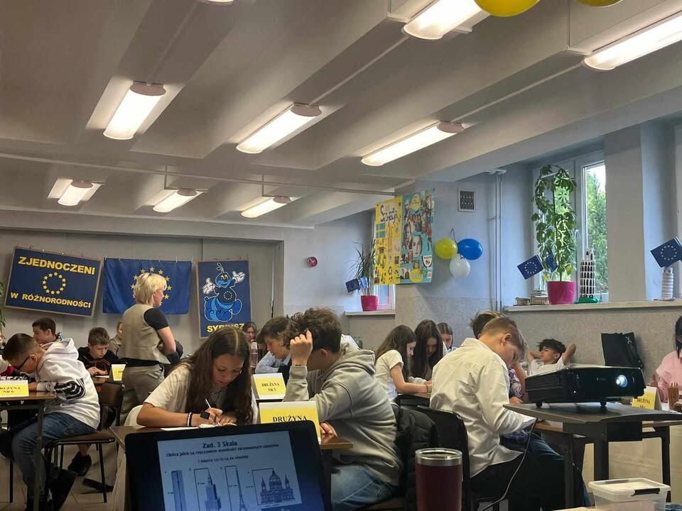 Dzieci siedzą przy stolikach.