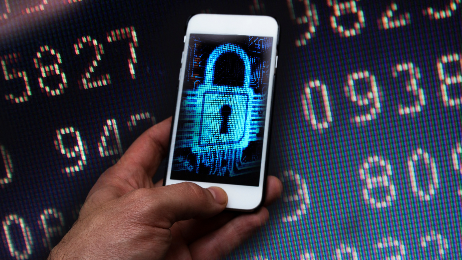 Na wyświetlaczu telefonu widoczna zamknięta kłódka. W tle na elektronicznej tablicy wyświetlane liczby.