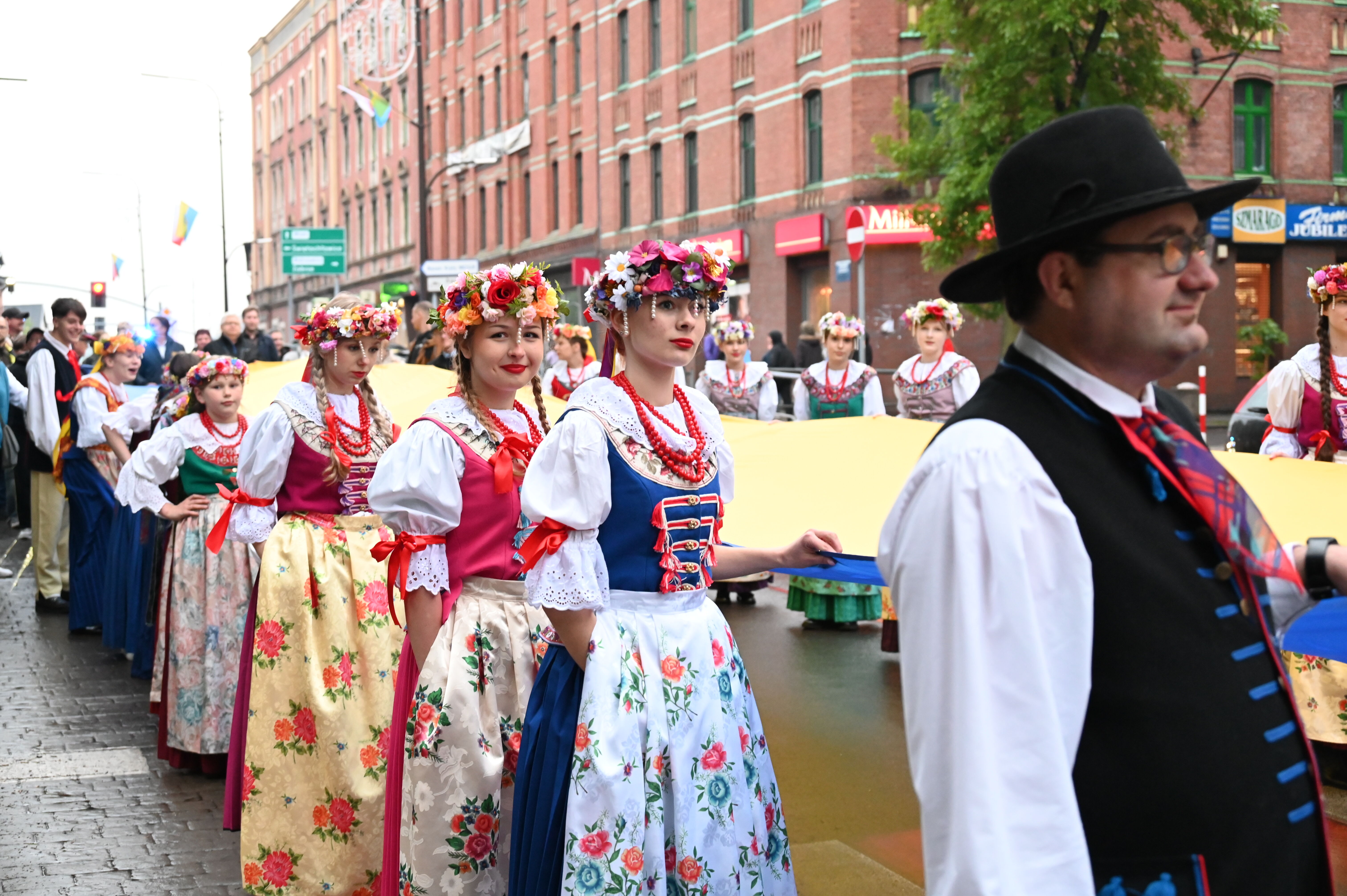 kobiety i mężczyźni w strojach śląskich idą ulicą miasta trzymając flagę śląską
