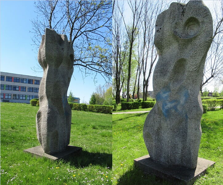 Dwie betonowe pionowe rzeźby stoją na zielonej trawie. W tle budynek.