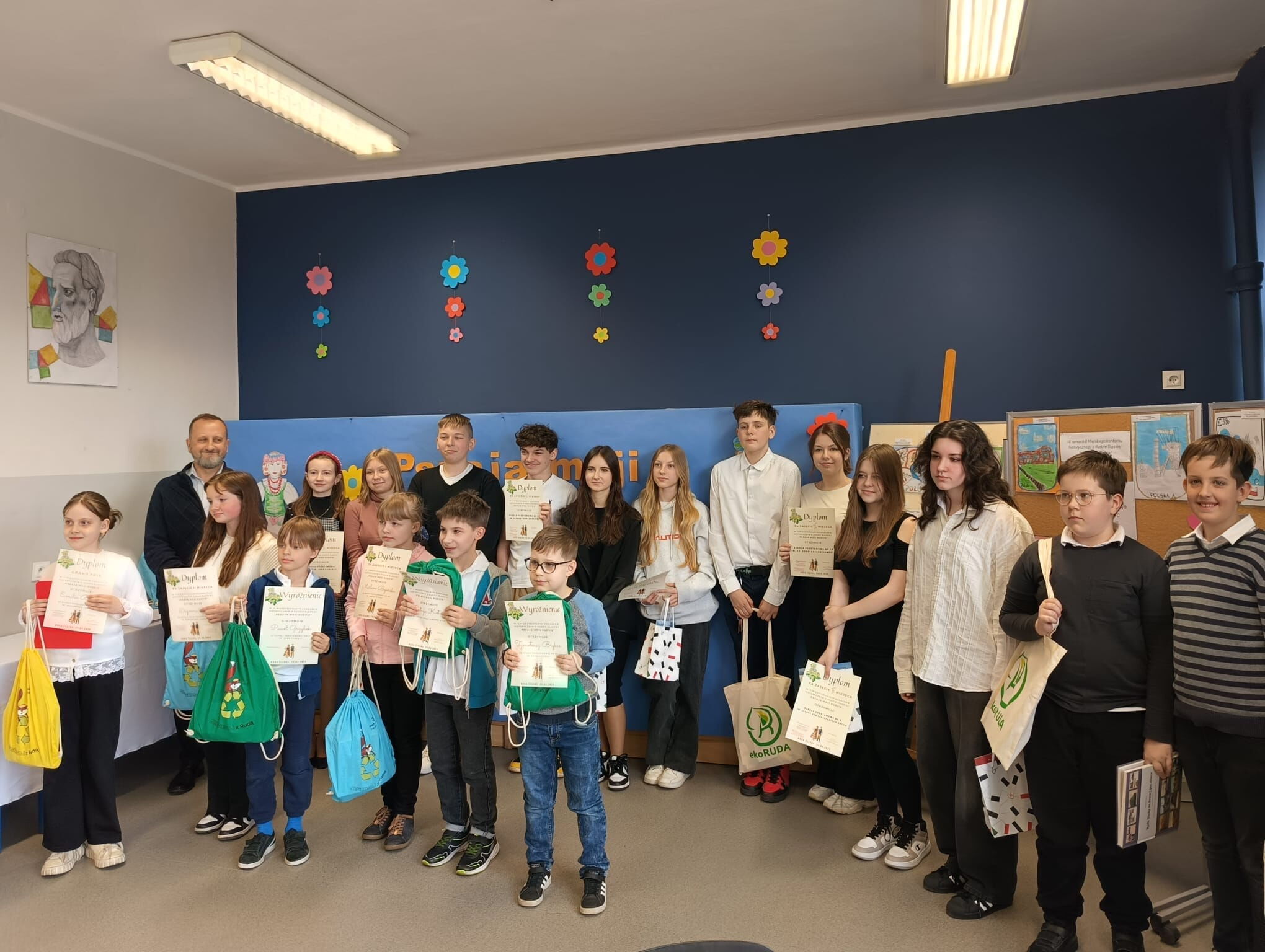 Grupa dzieci i dorosłych trzymająca w rękach dyplomy i nagrody/