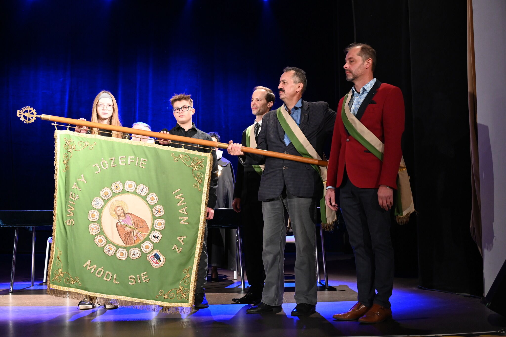 Kilka osób trzyma sztandar z patronem rzemieślników.