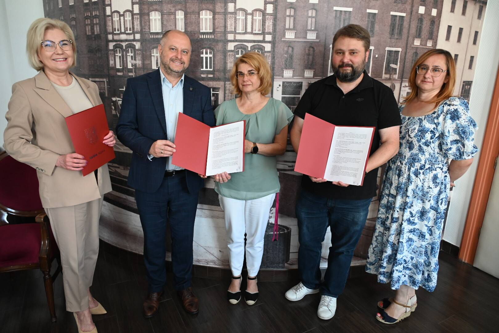 Grupa 4 osób prezentuje 2 egzemplarze w teczkach -  umowa podpisana