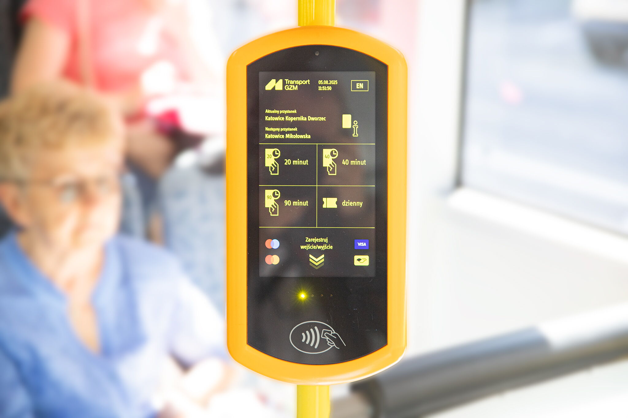 Mobilne urządzenie do zakupu biletów, w tle pasażerowie.