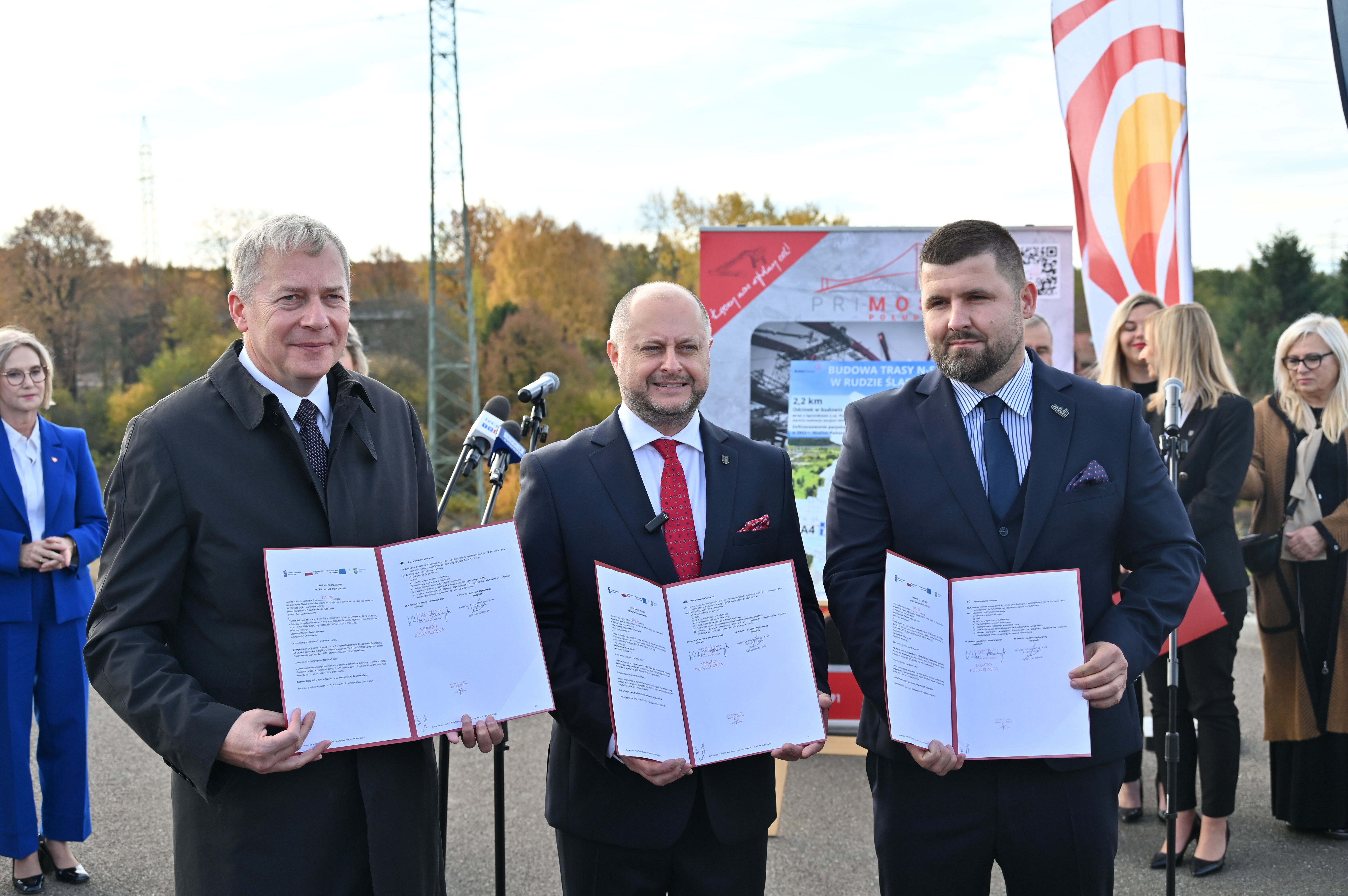 Trzy osoby prezentują tekst podpisanej umowy na budowę Trasy NS