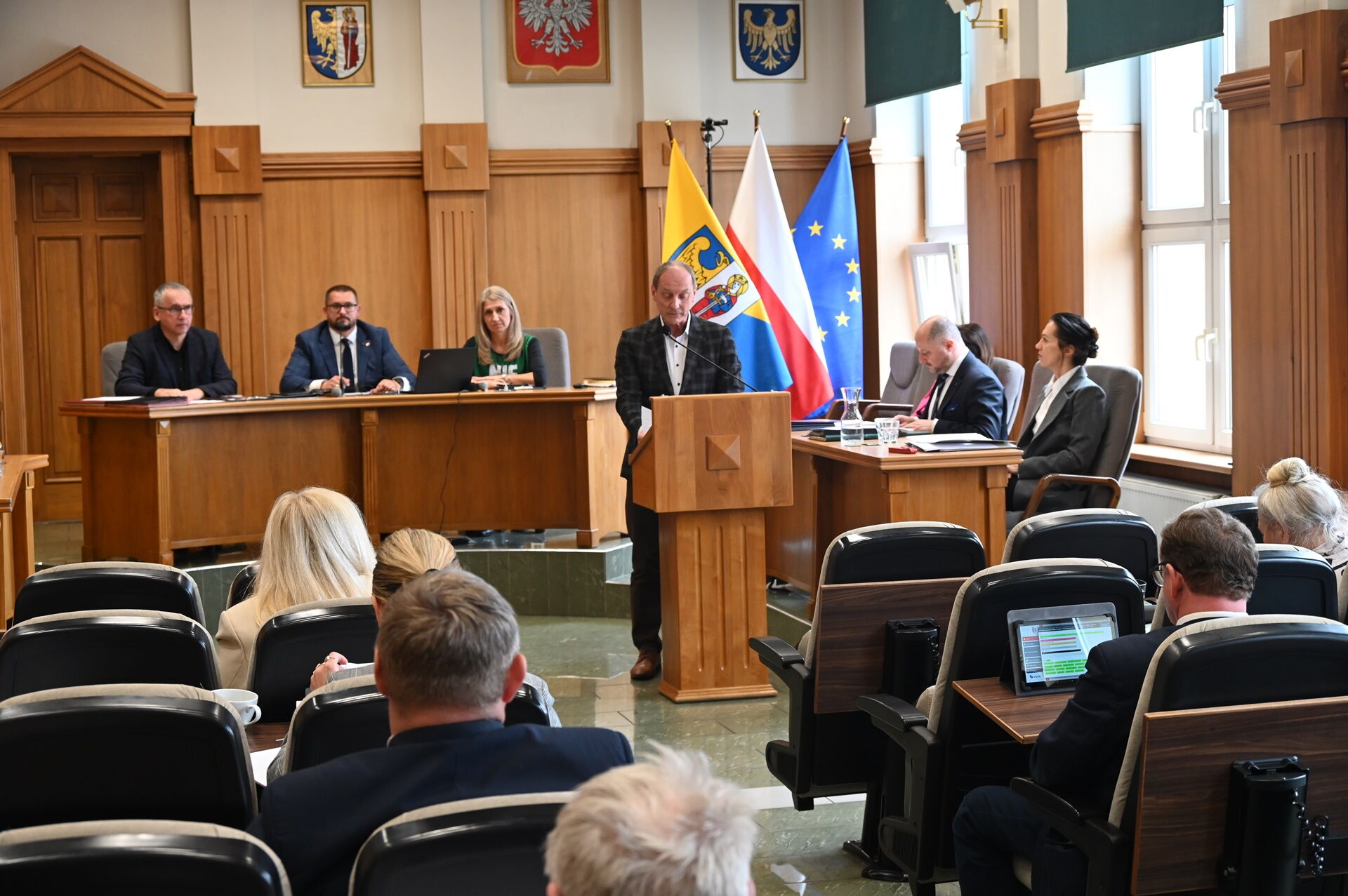 Widok sali sesyjnej. Przy mównicy mężczyzna w garniturze.