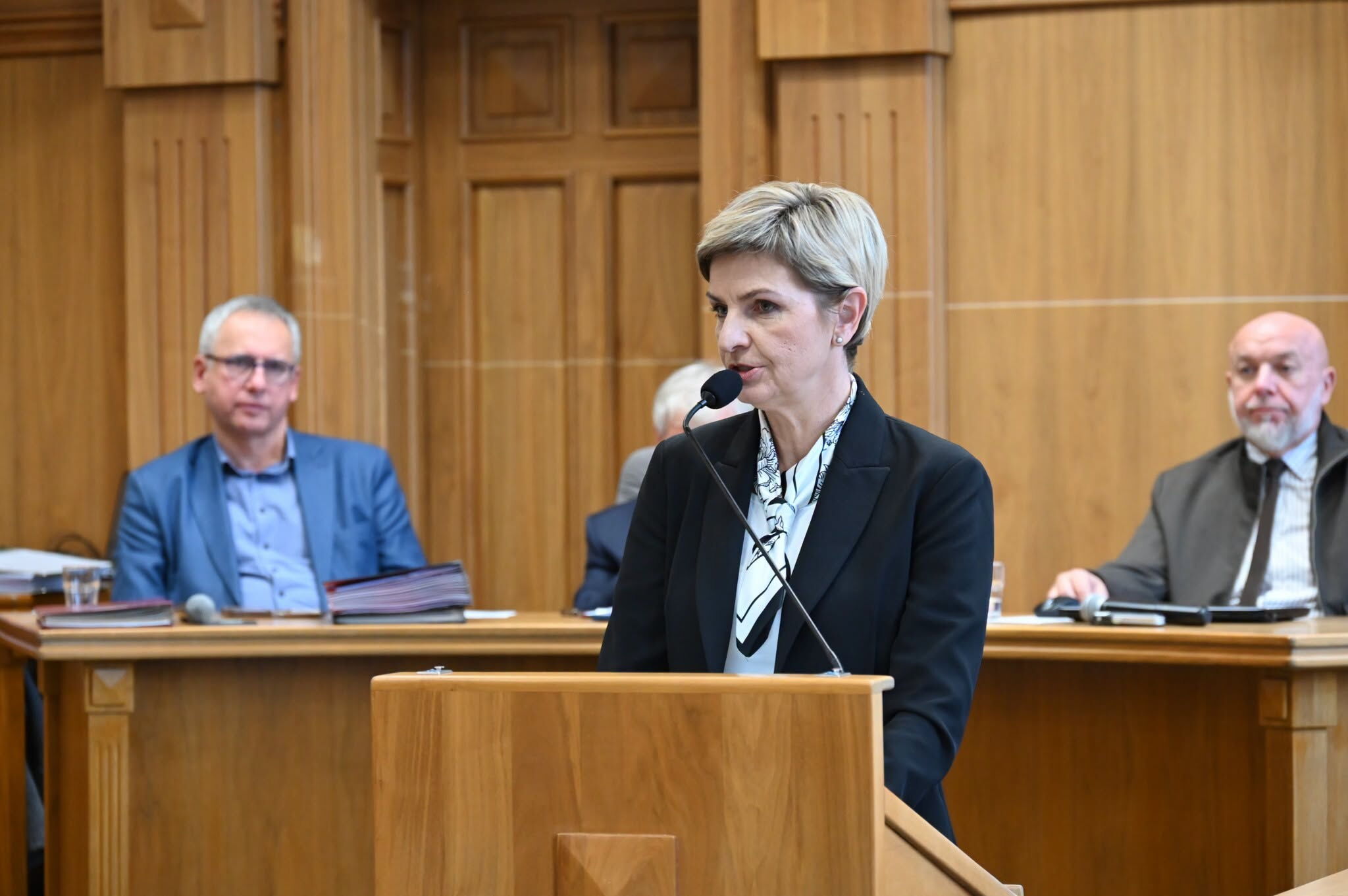 Sala sesyjna - przy mównicy kobieta. W tle trzech mężczyzn.