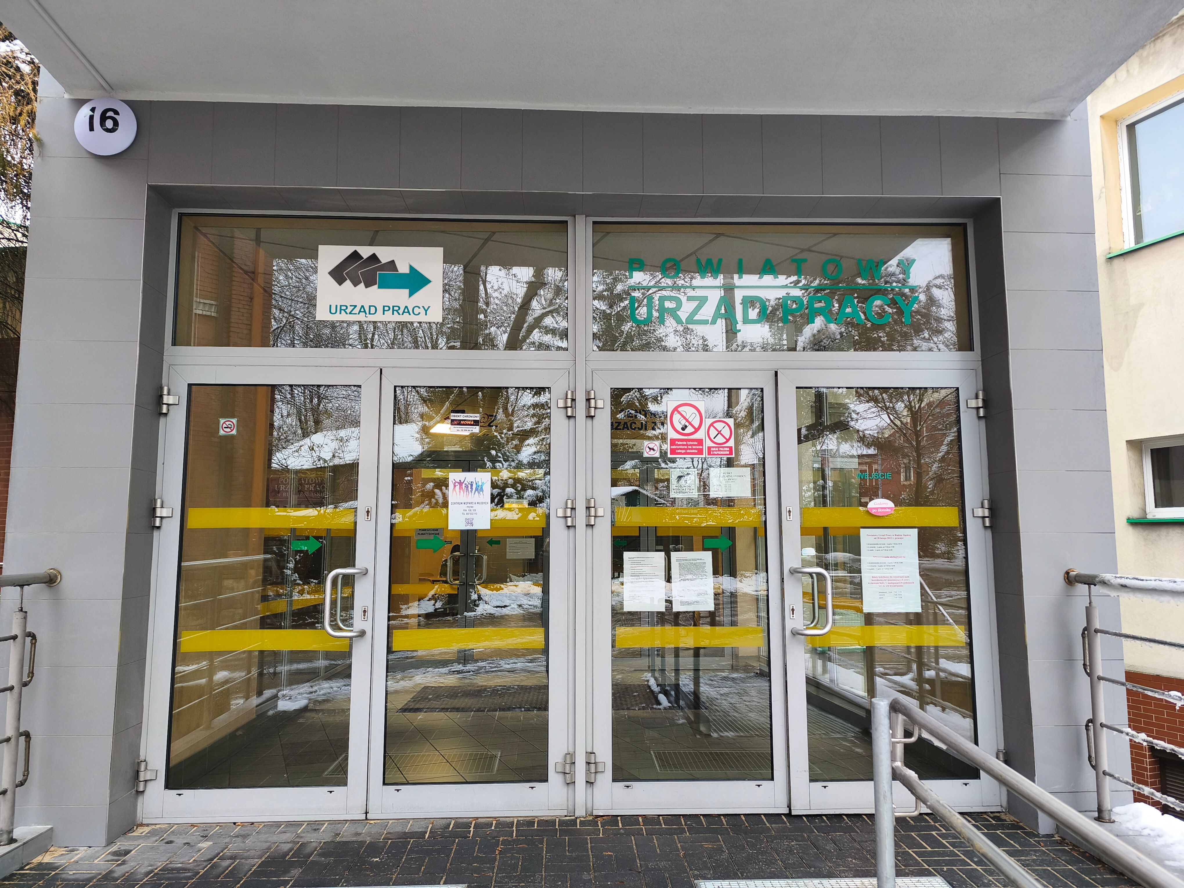 Duże, podwójne wejście do urzędu pracy w Rudzie Śląskiej. Drzwi są przeszklone i oklejone ogłoszeniami.