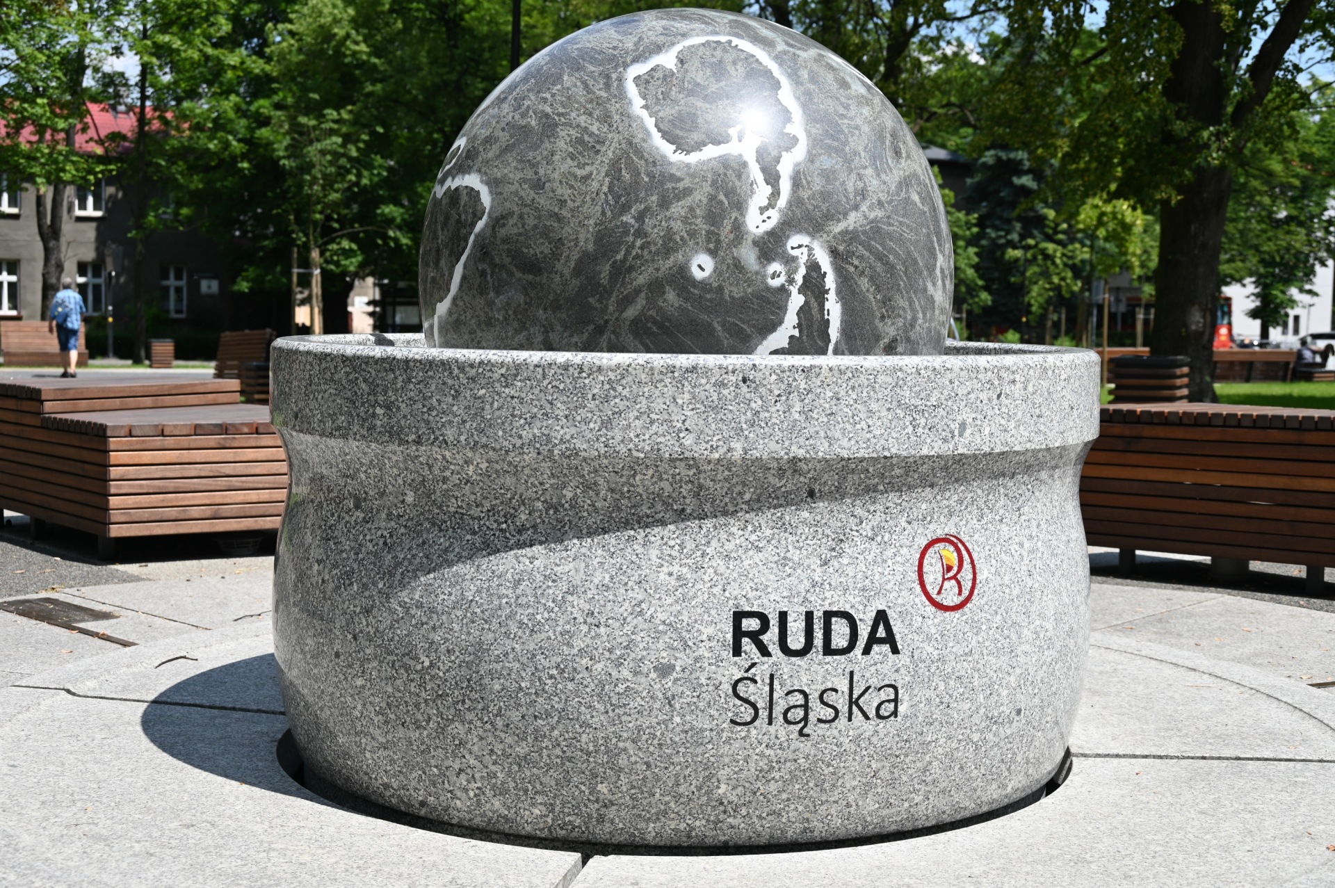 Kula ziemska betonowym postumencie z logo Rudy Śląskiej. W tle ławki i drzewa.