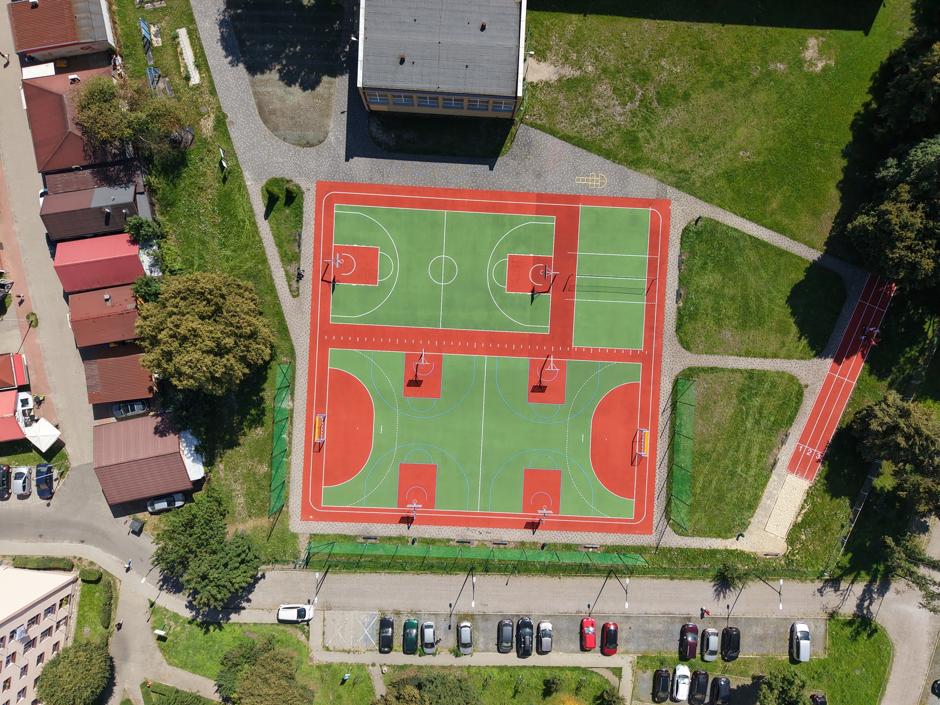 Widok z góry na odnowione boiska szkolne. Obok parking i zabudowa miejska.