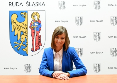 Kobieta w niebieskim żakiecie, w tle ścianka z herbem Rudy Śląskiej